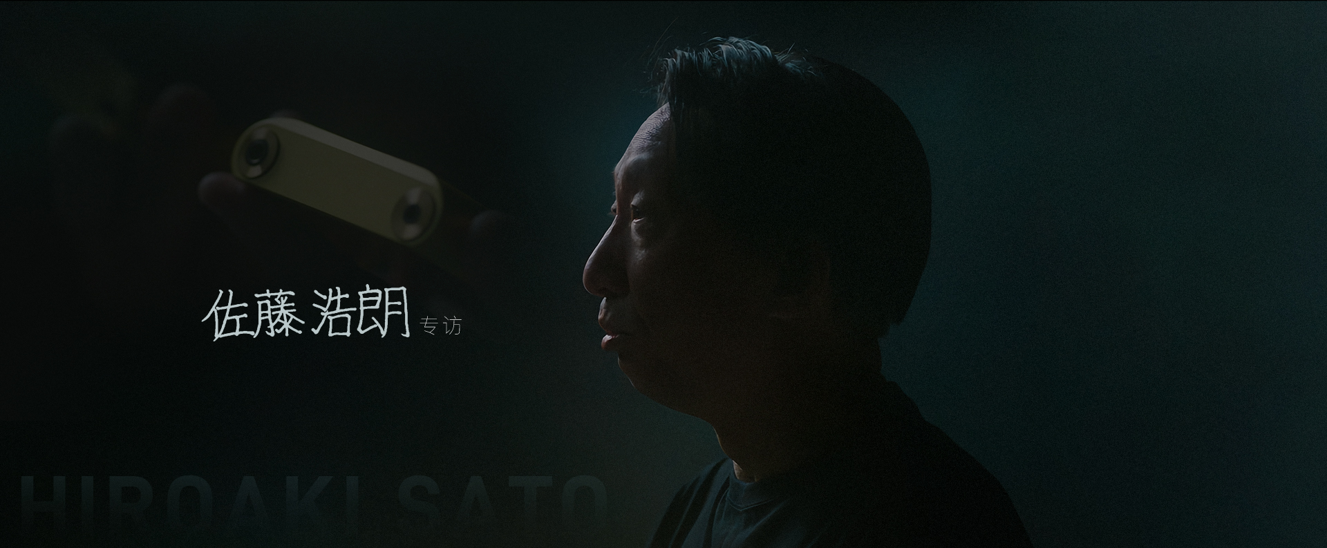 佐藤浩朗专访场景，昏暗光线中的侧脸，手持金色播放器